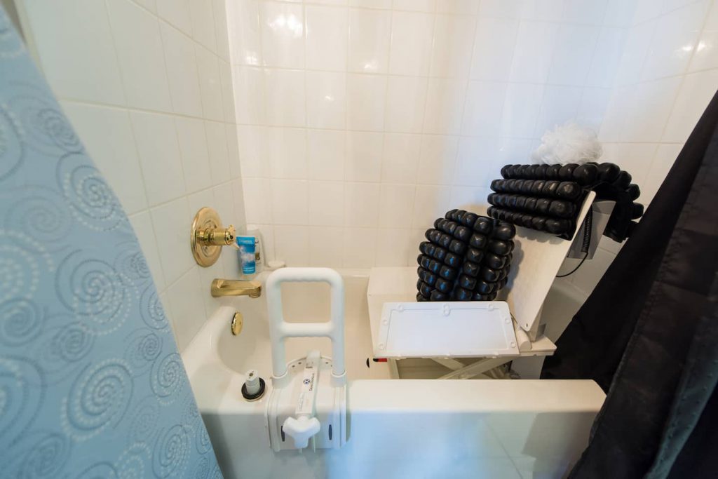 The shower area contains a tub and tiled surround. The homeowner does self-transfers, and uses a bench seat. Roho cushions dry easily and can be used to discourage pressure wounds. The adjustable grab bar works on most tubs.