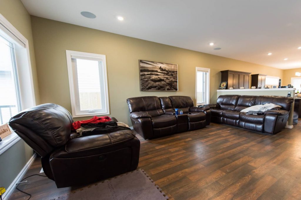 Vinyl plank flooring runs into the living room. Leather furniture is easy to transfer onto, and has the added bonus of easy upkeep. Low windows have coverings that are remotely operated.