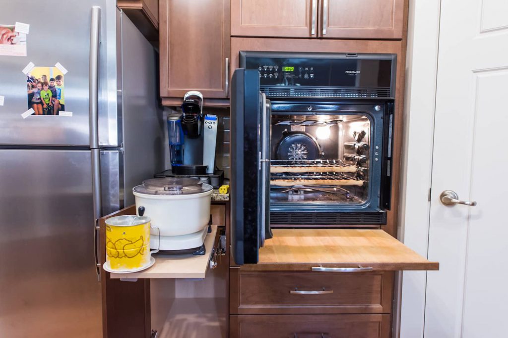 The wall mount oven is necessary for the homeowner's ability to work in the kitchen. The side opening door, and pull out cutting board underneath work great for removing and placing hot items. The pull out cupboard shelves to the left of the oven offer an added workspace for a kitchen appliance. The electrical outlet is inside the cupboard.